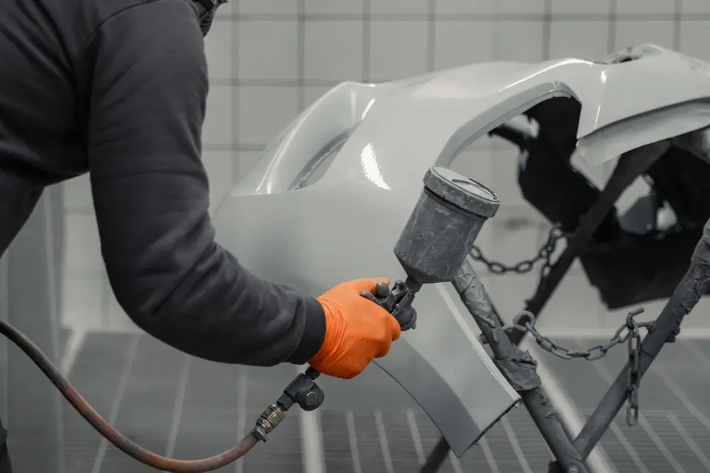 Worker in safety clothing and orange gloves spray painting a vehicle for auto body paint repair in Eugene, OR