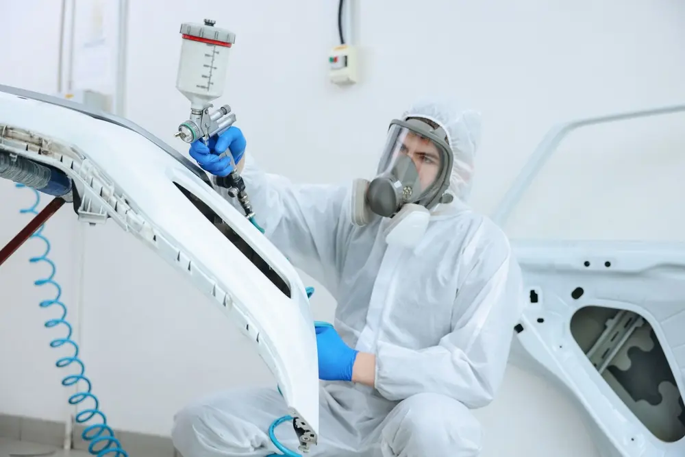 Worker in a white safety clothing and mask spray painting a vehicle for custom paint work in Eugene, OR