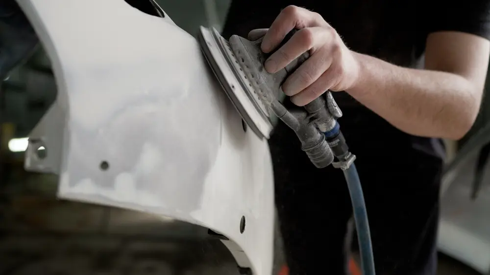 Worker in black clothing buffing a vehicle bumper for auto body repair in Eugene, OR